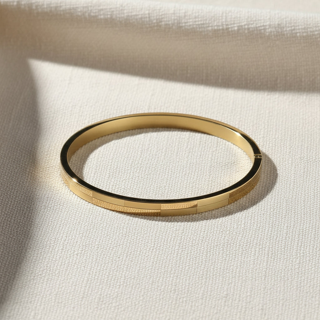A realistic, natural daylight flat lay photograph of the premium gold plated oval brick textured block bracelet, sized specifically for thin wrists, resting beautifully on a textured cream linen cloth.