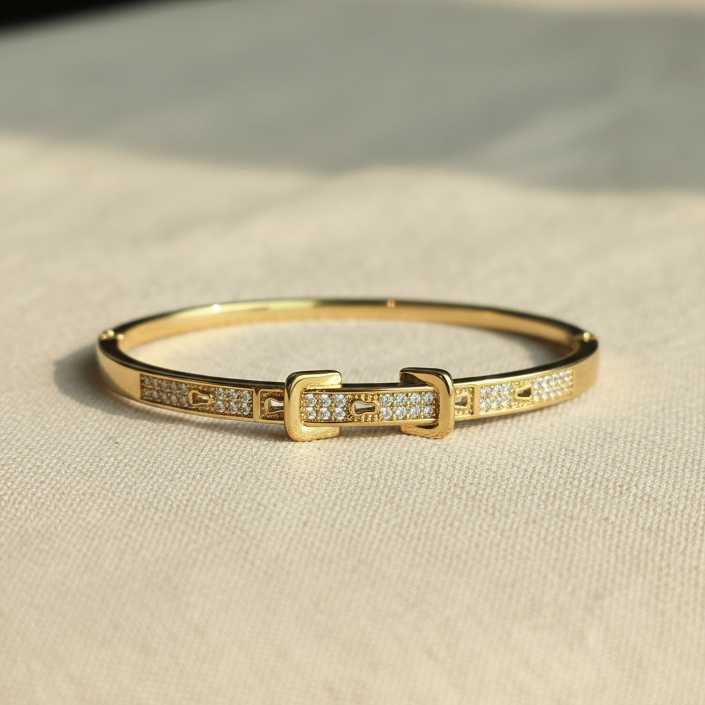 A realistic, natural daylight flat lay photograph of the premium gold plated belt buckle crystal lock bracelet resting naturally on a textured cream linen cloth.