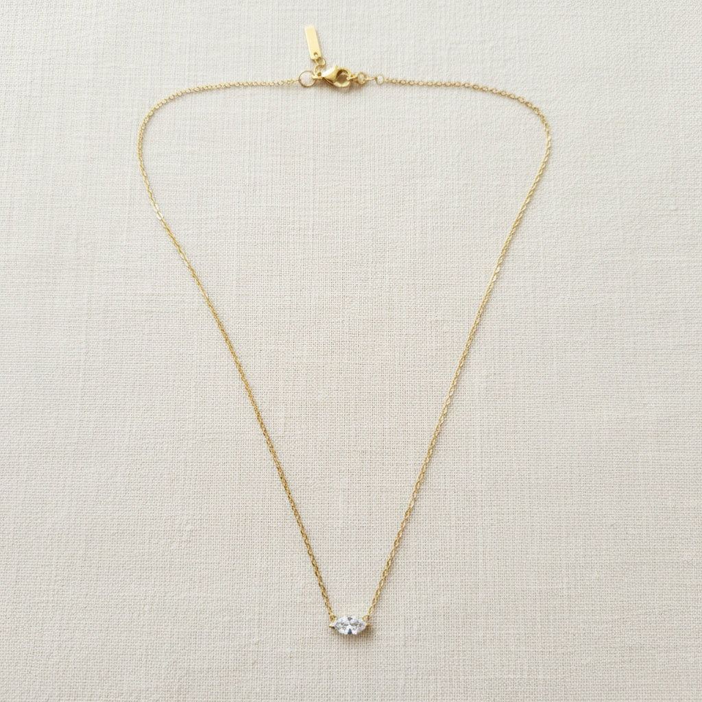 A realistic photograph of the ultra-fine 18K gold starburst necklace resting naturally on a textured cream linen cloth under natural light.