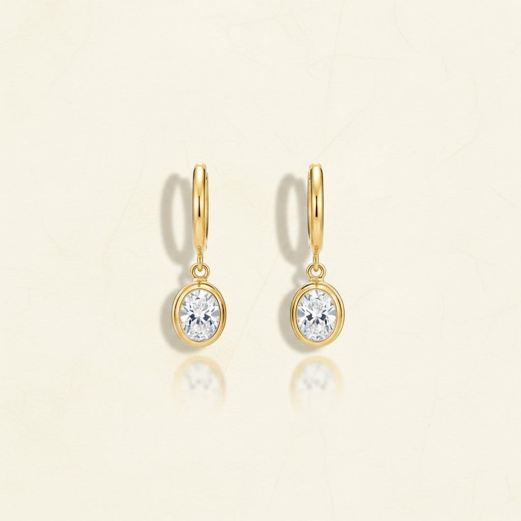 Macro detail shot focusing on the bezel-set oval crystal and the secure hinged closure of the gold earring.