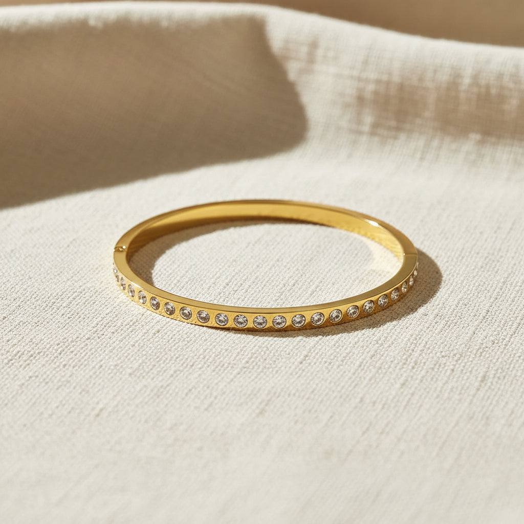 A realistic, natural daylight flat lay photograph of the premium gold plated single row crystal eternity bracelet resting naturally on a textured cream linen cloth.