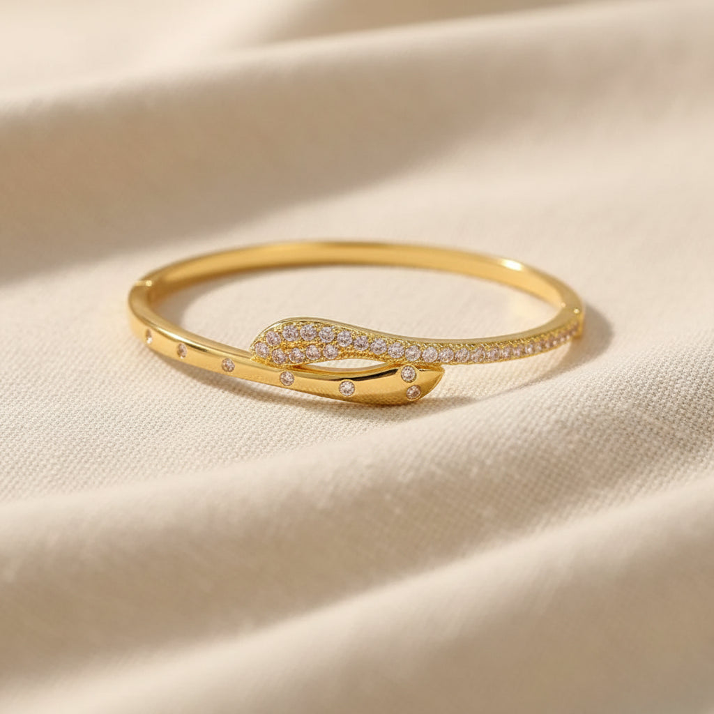 A realistic, natural daylight flat lay photograph of the premium gold plated serpentine crossover kada bangle resting beautifully on a textured cream linen cloth.