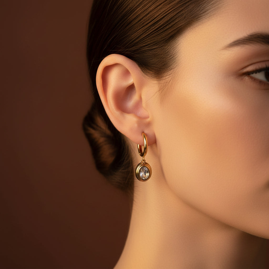 A close-up lifestyle shot of a woman wearing the 18K gold plated oval crystal drop huggie earrings.