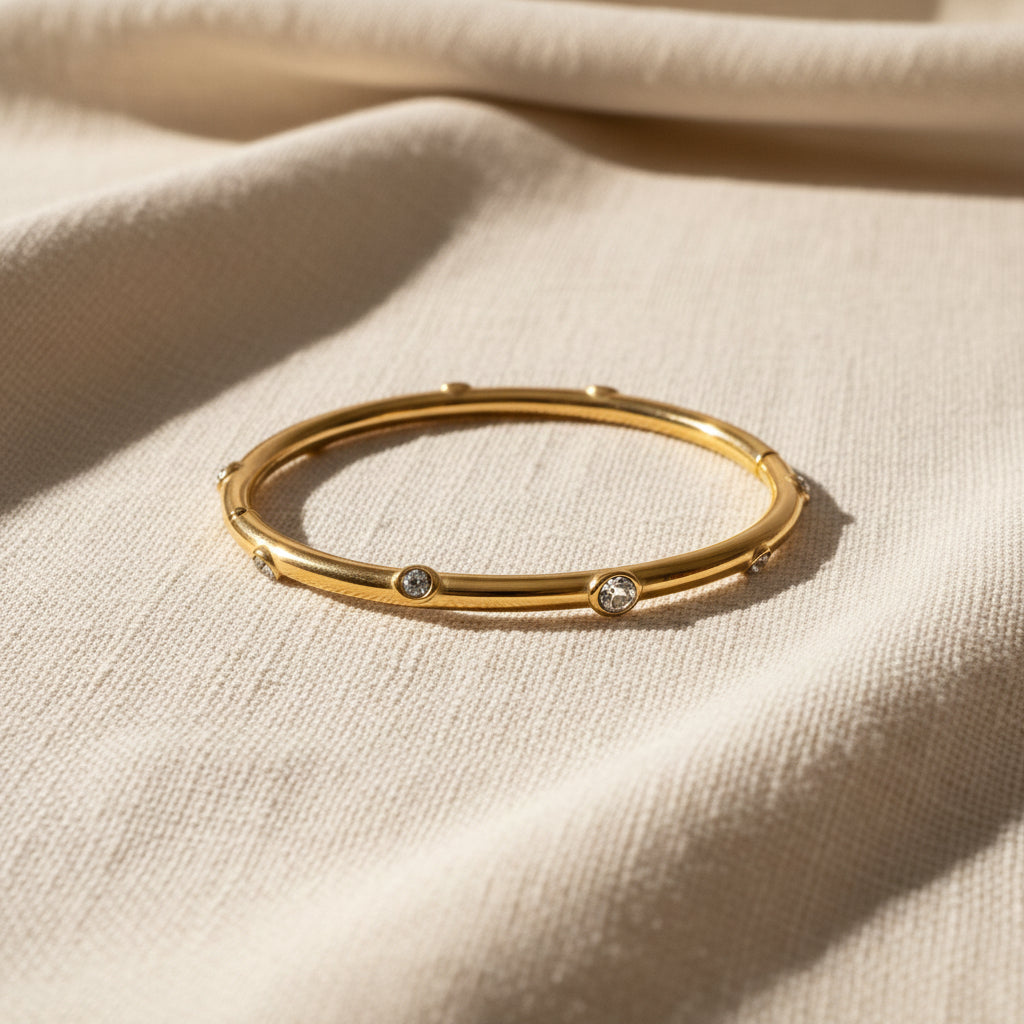 Gold bracelet with embedded stones on a white cushioned surface