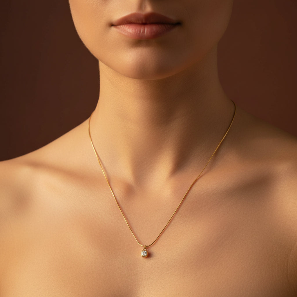 A detailed, realistic photograph focusing on a woman's neck, wearing the 18K gold plated cushion-cut solitaire necklace under warm golden lighting against a solid deep cocoa brown background.