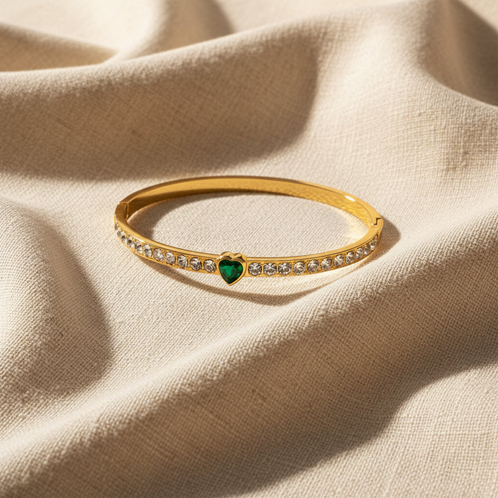 Gold bracelet with a green heart charm on a white background