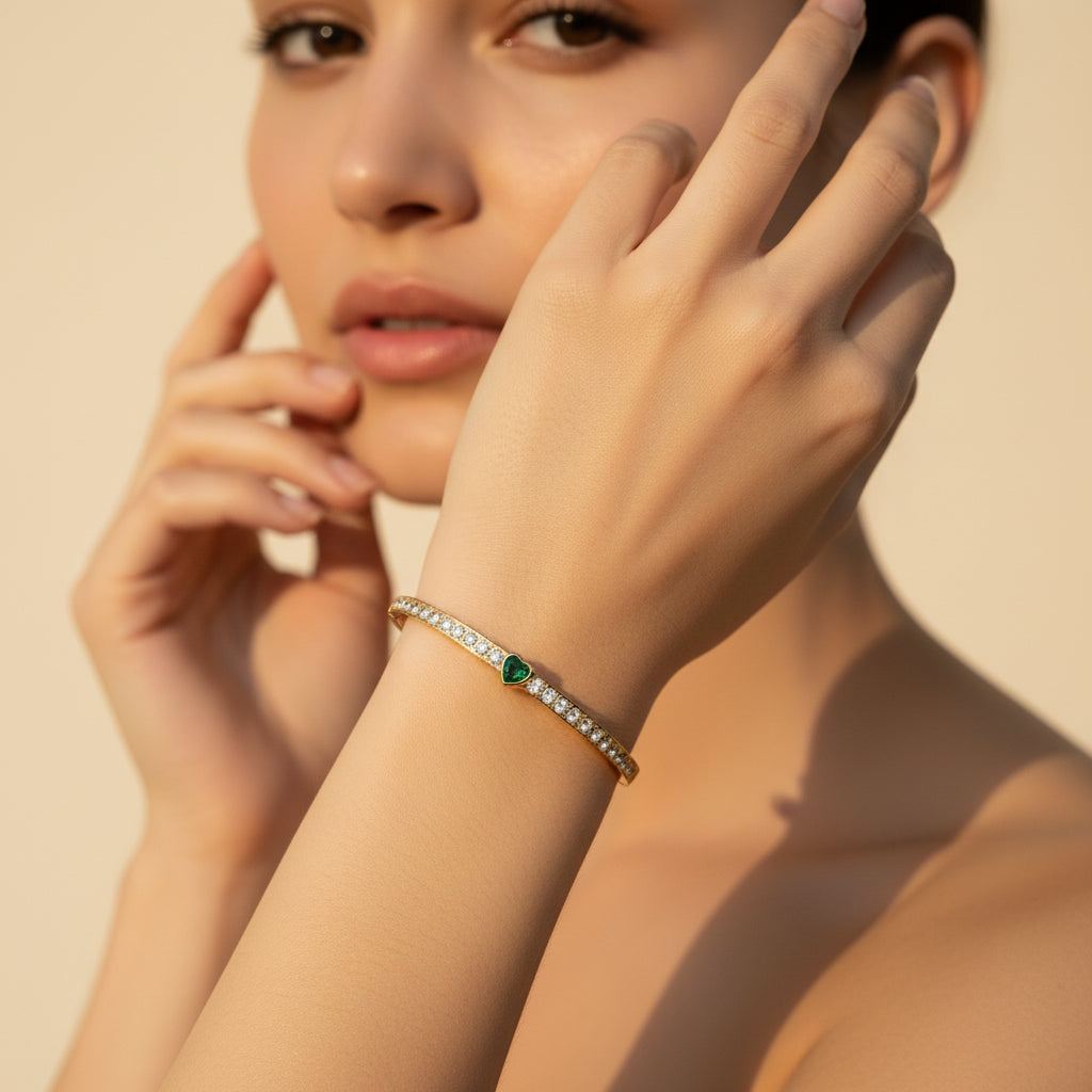 Gold bracelet with a green heart charm on a white background