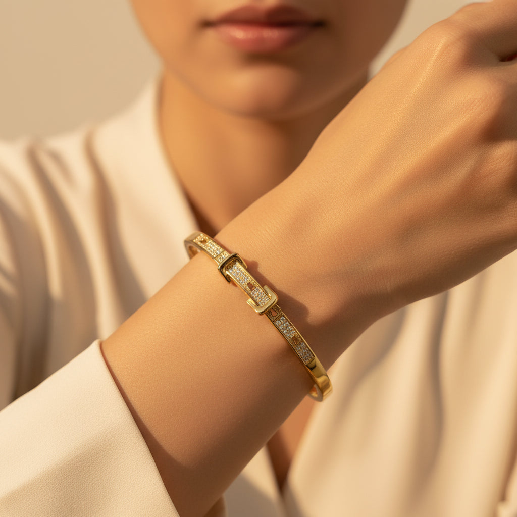 A standing profile photograph of a model (face half visible), highlighting the unique gold belt buckle crystal bracelet on her wrist under warm golden lighting against a light #f5f3eb cream background.
