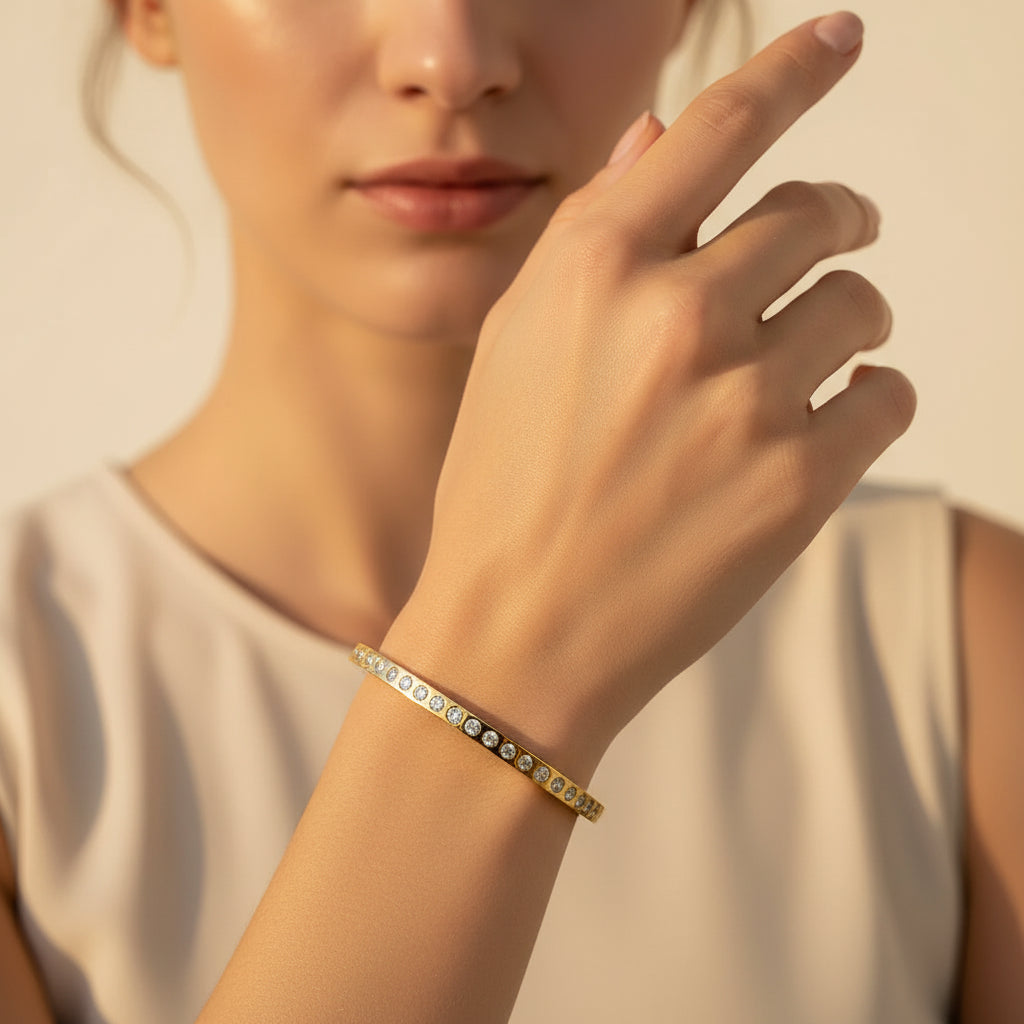A standing profile photograph of a model (face half visible), highlighting the sleek gold continuous crystal eternity bracelet on her wrist under warm golden lighting against a light #f5f3eb cream background.