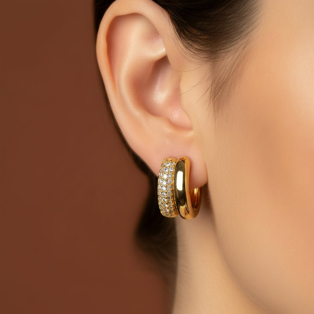 Zoomed-in flat shot focusing closely on a model's ear wearing the gold multi-layer split band crystal huggie earrings under warm golden lighting against a rich #5b3b3a brown background.