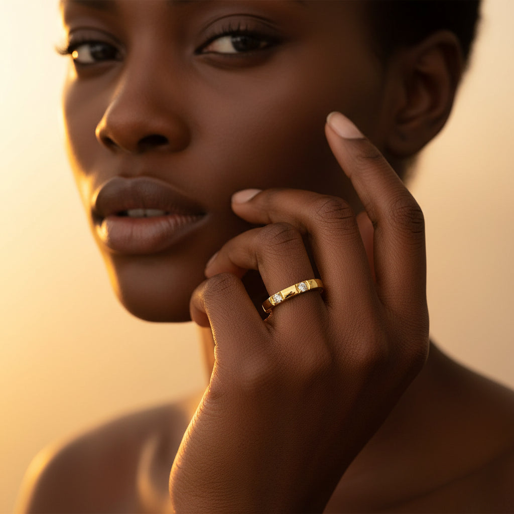 A stunning high-end e-commerce editorial photograph of a beautiful Black beauty model under warm golden lighting, with her face visible and the focus zoomed in tightly on the gold flat-edge triple crystal stacking ring without changing its design.