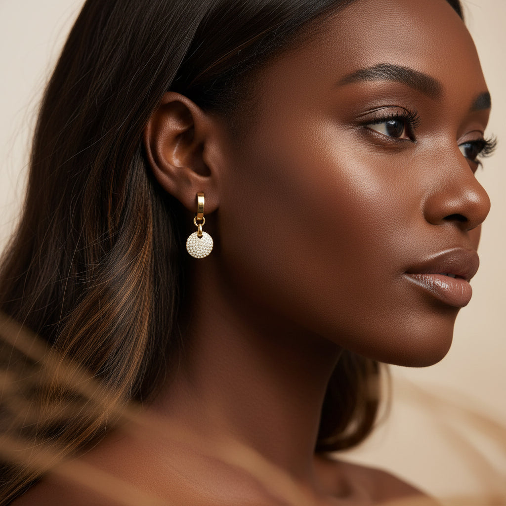 Close-up side profile photograph of a model wearing the gold geometric crystal disc drop earrings under warm golden lighting against a minimal cream background.