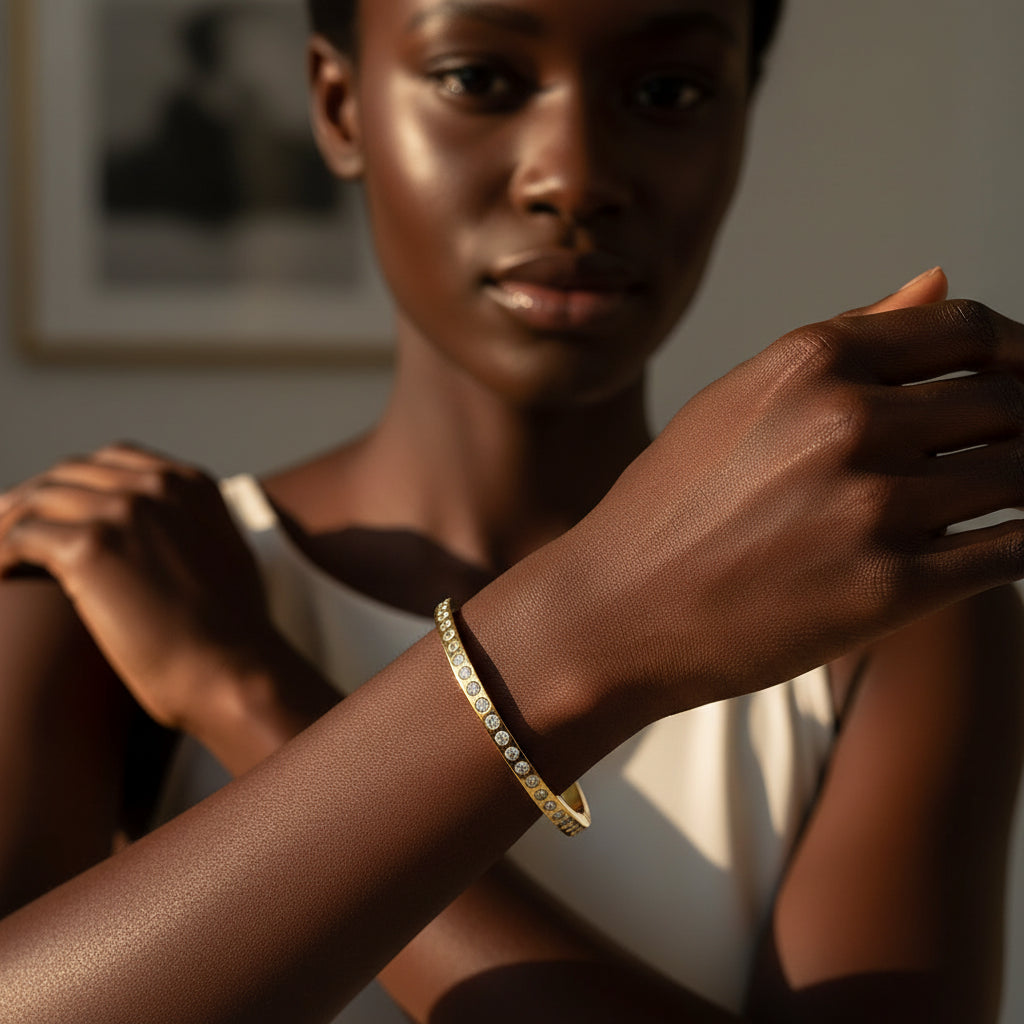 A stunning high-end e-commerce editorial photograph of a beautiful Black beauty model under warm golden lighting, with her face fully visible and the focus centered sharply on the regular size gold single row crystal eternity kada bracelet.