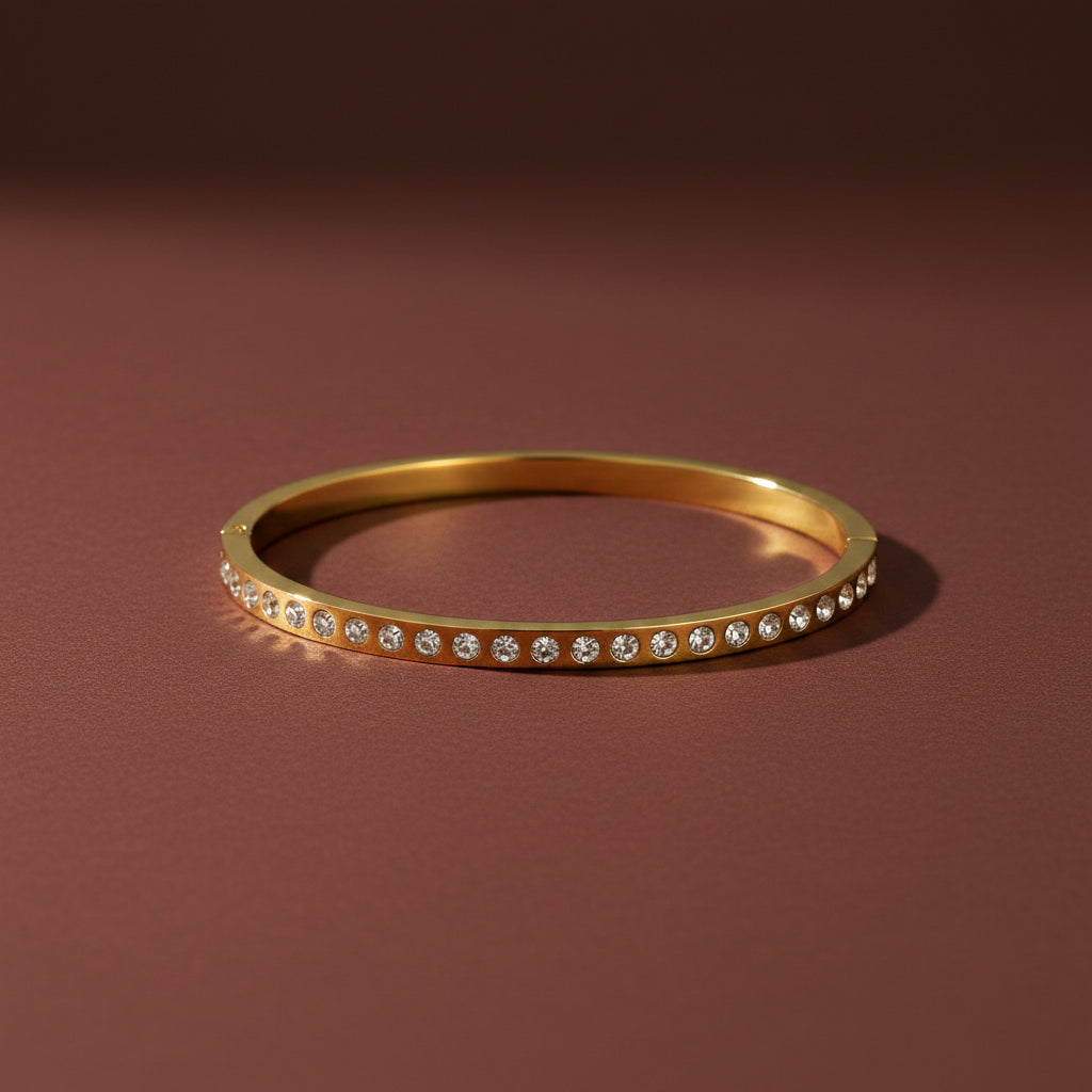 A professional high-angle catalogue shot of the gold plated single row crystal eternity kada bangle in standard size, isolated with simple shadows on a rich #5b3b3a brown background