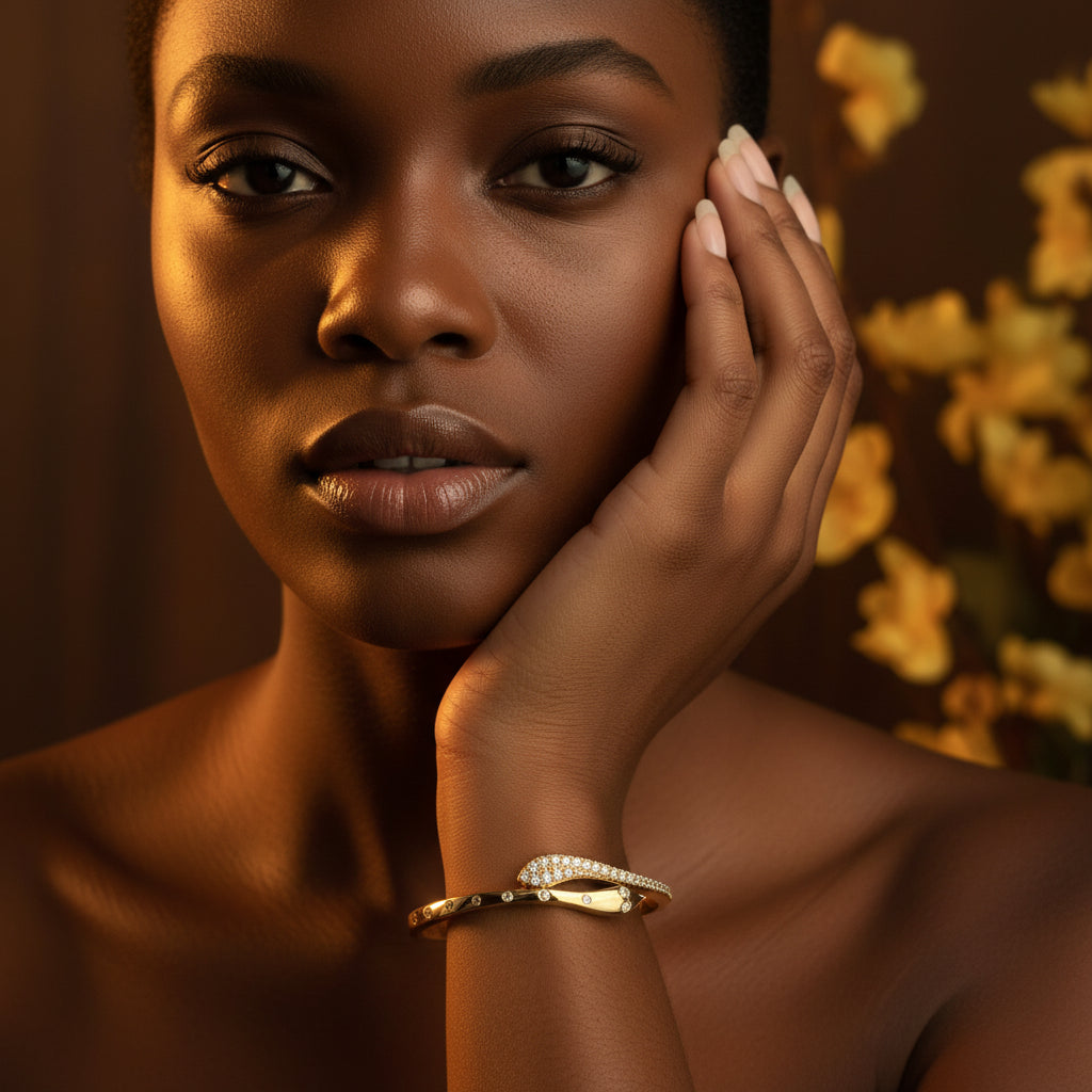 A stunning high-end e-commerce editorial photograph of a beautiful Black beauty model under warm golden lighting, with her face fully visible and the focus centered sharply on the gold snake crossover kada bangle on her arm.