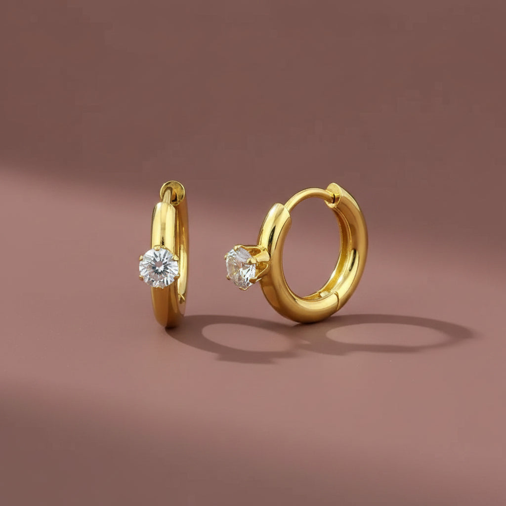 18K gold plated solitaire huggie earrings with Cubic Zirconia on a luxury brown catalogue background.