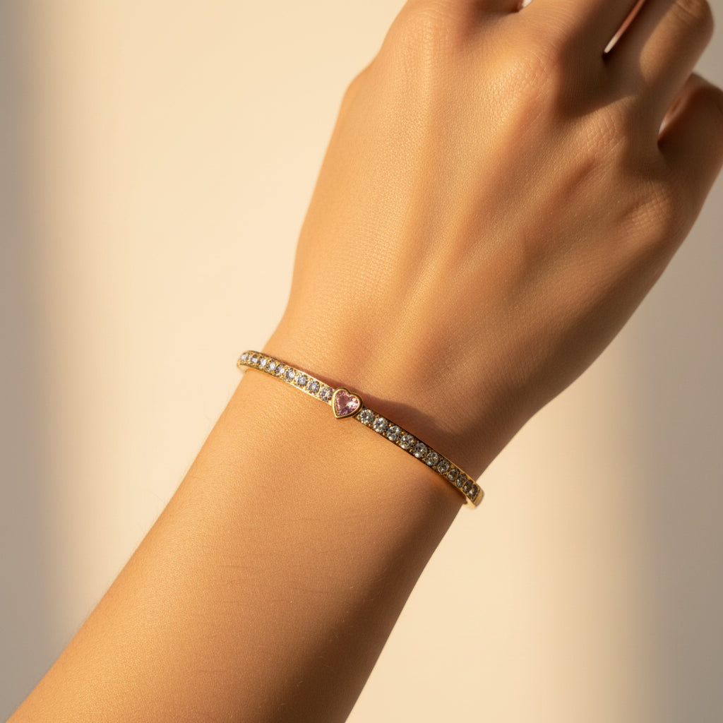 A model's wrist wearing the Pink Heart Stone Gold Bangle to showcase its soft color and elegant, structured profile.
