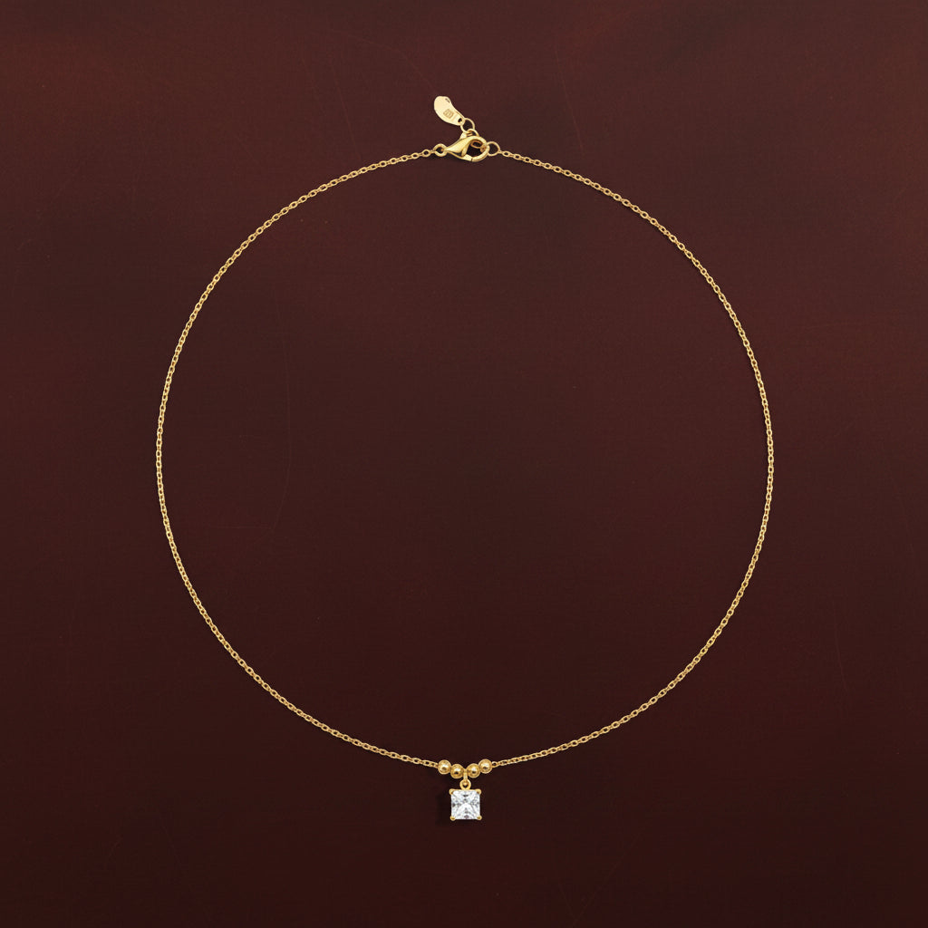 An appealing lifestyle photograph of a model in a pose with her hand, showcasing the princess-cut square solitaire pendant necklace under dramatic lighting against a minimal, light background.