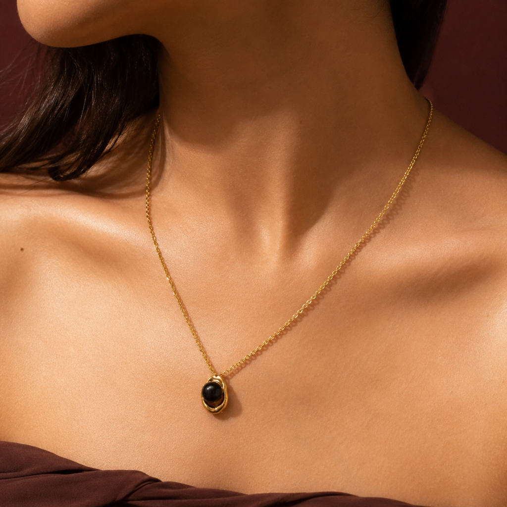 Woman wearing a gold necklace with a polished black stone pendant.