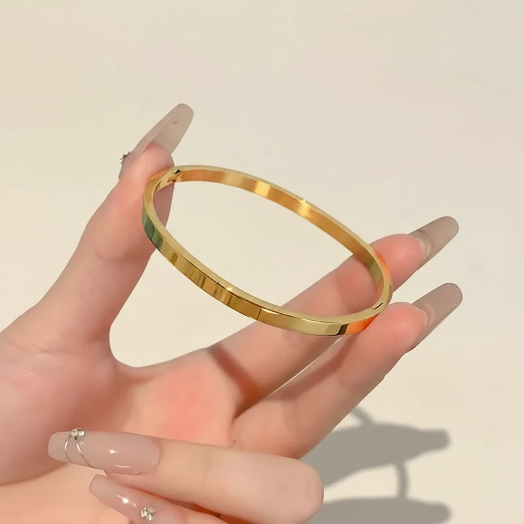 A professional standing catalogue view of the minimalist small size gold plated plain kada bangle, specifically for thin wrists, with simple shadows on a light cream background.