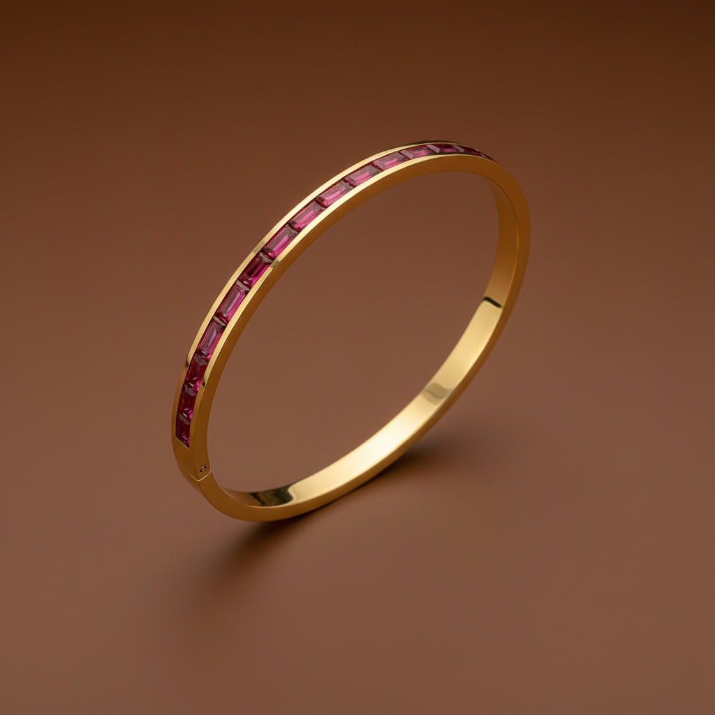 A close-up view of the Ruby Line Gold Bangle showcasing the deep red crystals and polished 18K gold-plated finish.