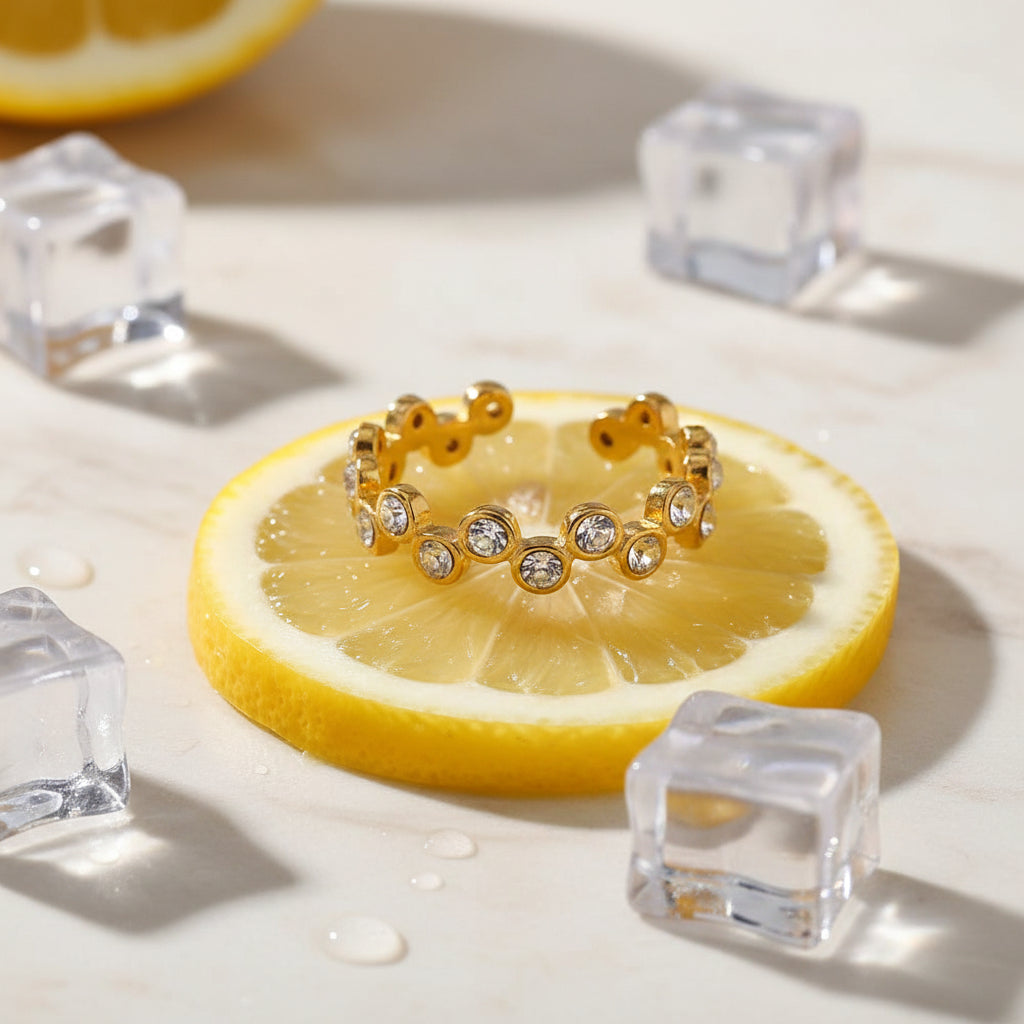 A high-end editorial lifestyle photograph showing a sharp, clearly visible gold zig-zag crystal ring placed on an appealing food item, with a half-visible model playfully acting as if she is eating it.