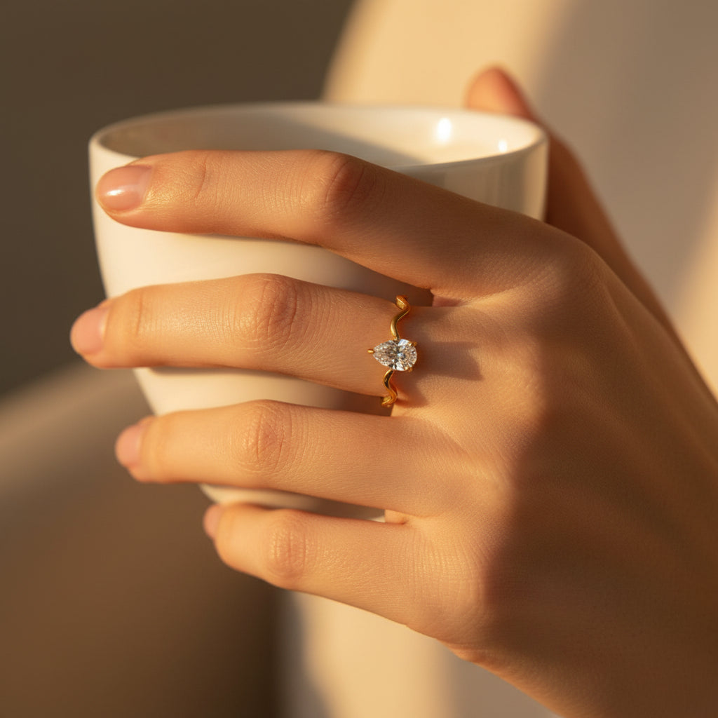 Close-up of a woman wearing the Serena Wave Pear Ring against a premium cream background.