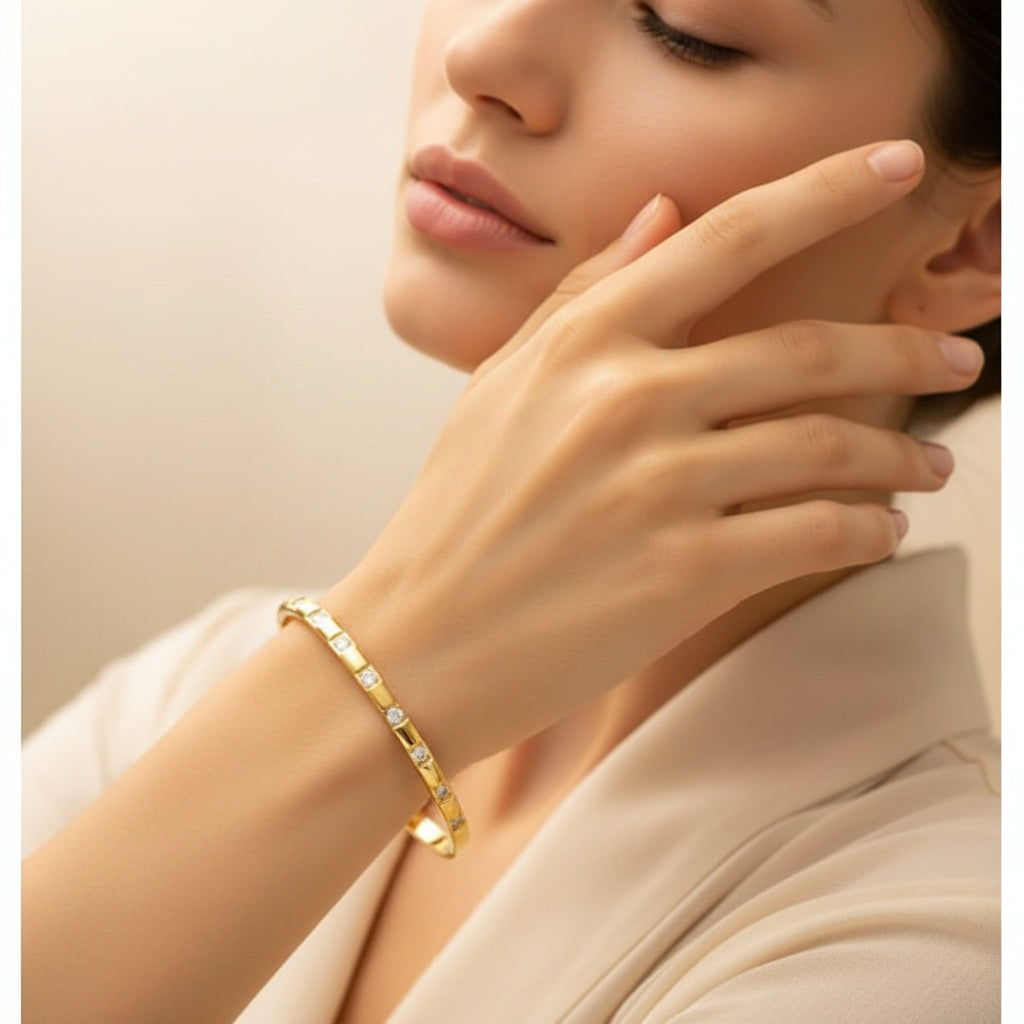 A standing profile photograph of a model (face half visible), showcasing the square-bordered crystal gold oval bracelet on her thin wrist under warm golden lighting against a cream background.