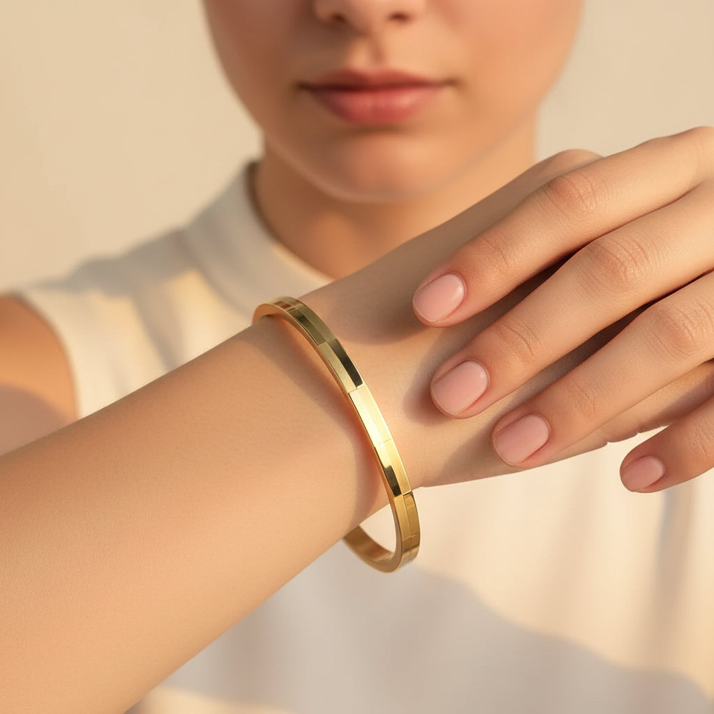 A standing profile photograph of a model (face half visible), showcasing the alternating matte and shiny brick gold oval bracelet on her thin wrist under warm golden lighting against a cream background.