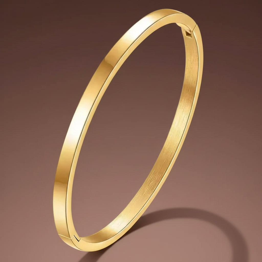 A professional high-angle catalogue shot of the plain oval gold plated stainless steel kada bangle, specifically sized for thin wrists, isolated on a deep cocoa brown background with clean shadows, as seen in IMG_5659.webp.