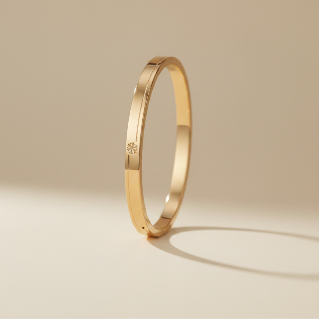 A professional standing catalogue view of the small size gold plated snowflake emblem bangle for thin wrists, with clean shadows on a light cream background.