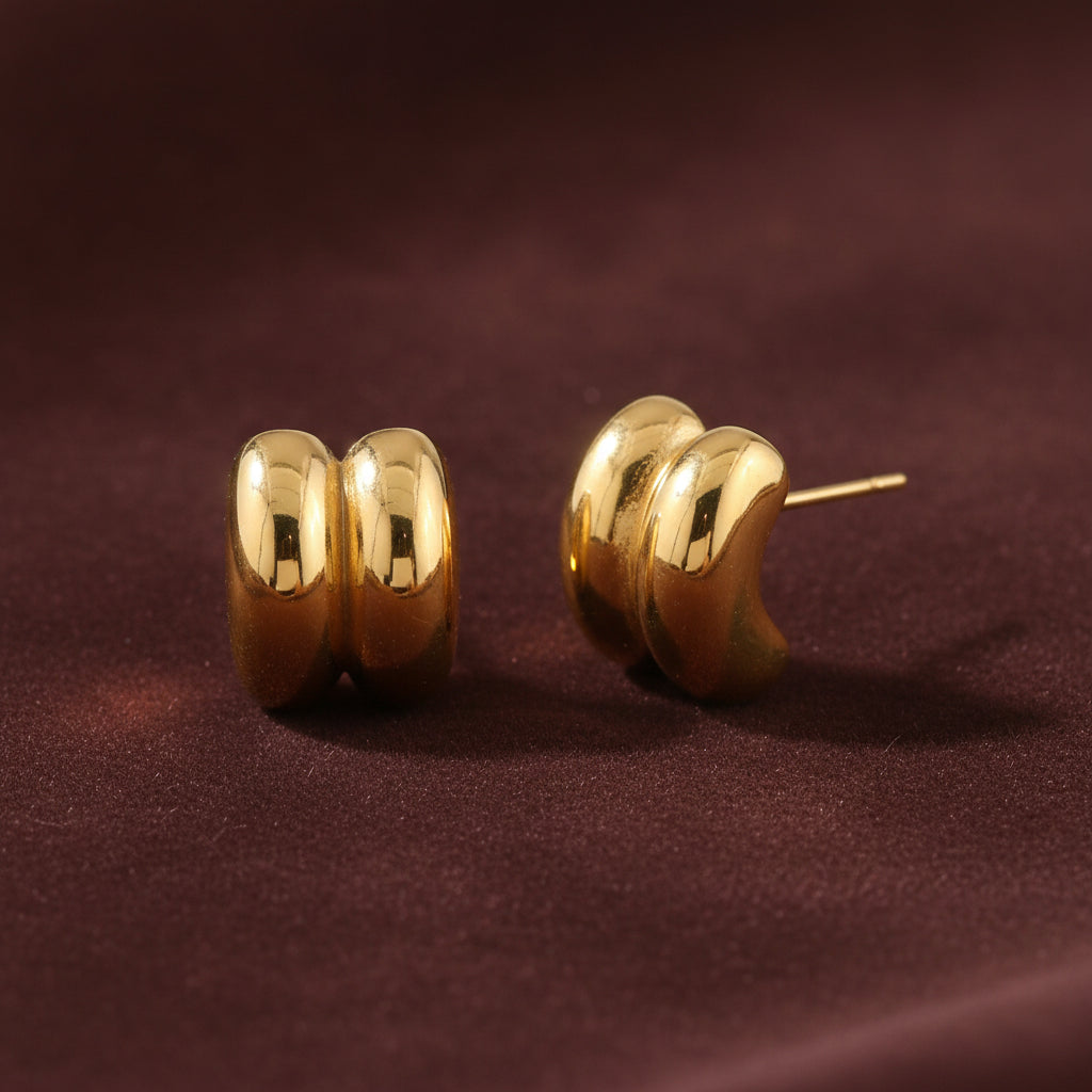 Professional catalogue flat lay of the Siren twin ribbed gold dome stud earrings with clean shadows on a rich brown background.