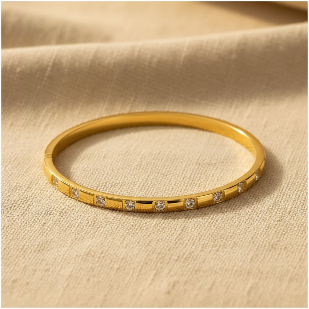 A realistic, natural daylight flat lay photograph of the premium gold plated oval block-station crystal bracelet, sized specifically for thin wrists, resting beautifully on a textured cream linen cloth.