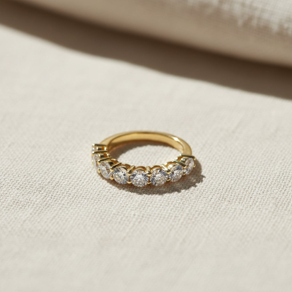 A realistic, natural daylight flat lay photograph of the premium gold seven stone shared prong crystal ring resting beautifully on a textured cream linen cloth.