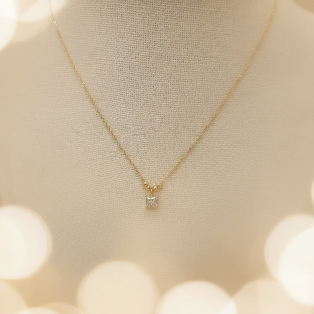 A realistic photograph of the ultra-fine 18K gold square crystal pendant necklace resting naturally on a textured cream linen cloth under natural light.