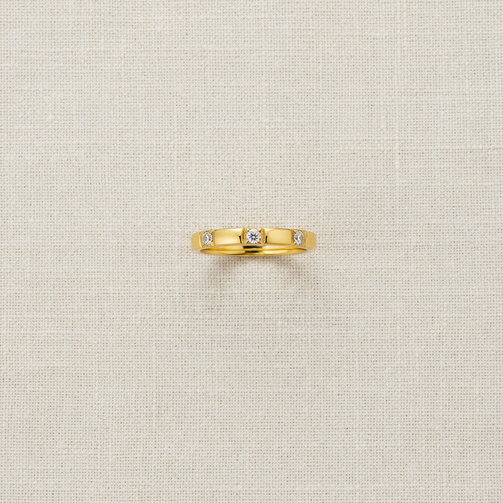 A realistic, natural daylight flat lay photograph of the premium gold flat edge triple crystal stacking ring with smooth square bezel settings resting beautifully on a textured cream linen cloth.