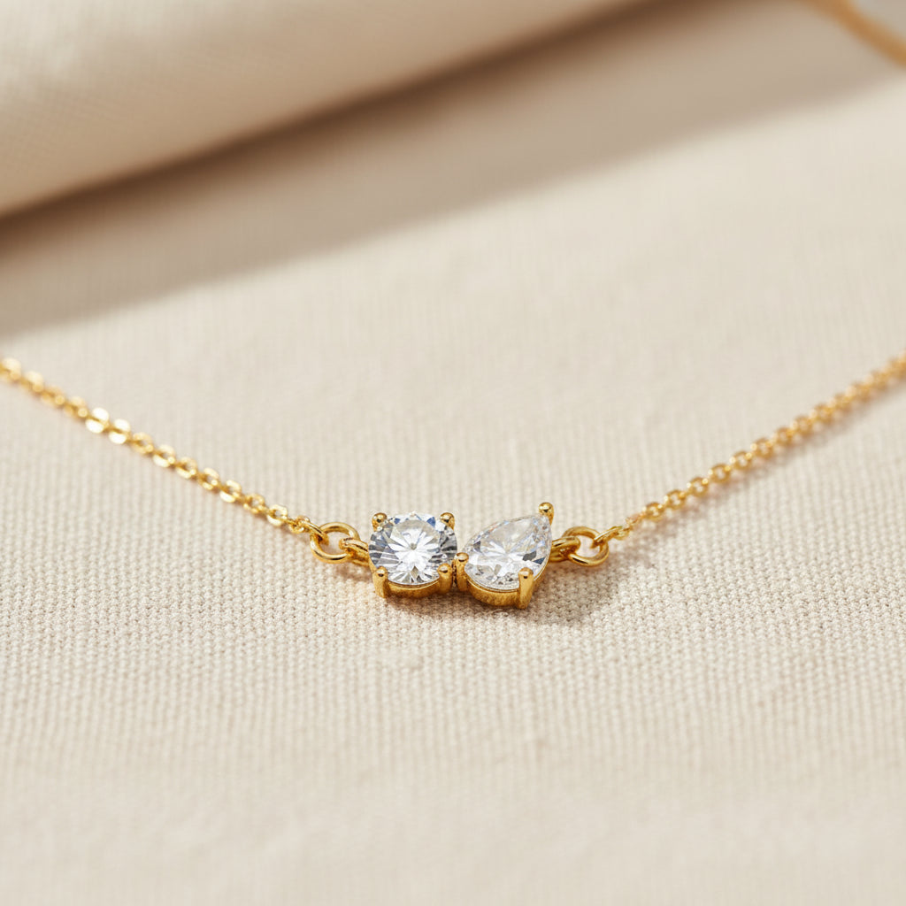 A realistic, natural daylight flat lay photograph of the premium gold chain with round and teardrop crystal cluster pendant resting beautifully on a textured cream linen cloth.