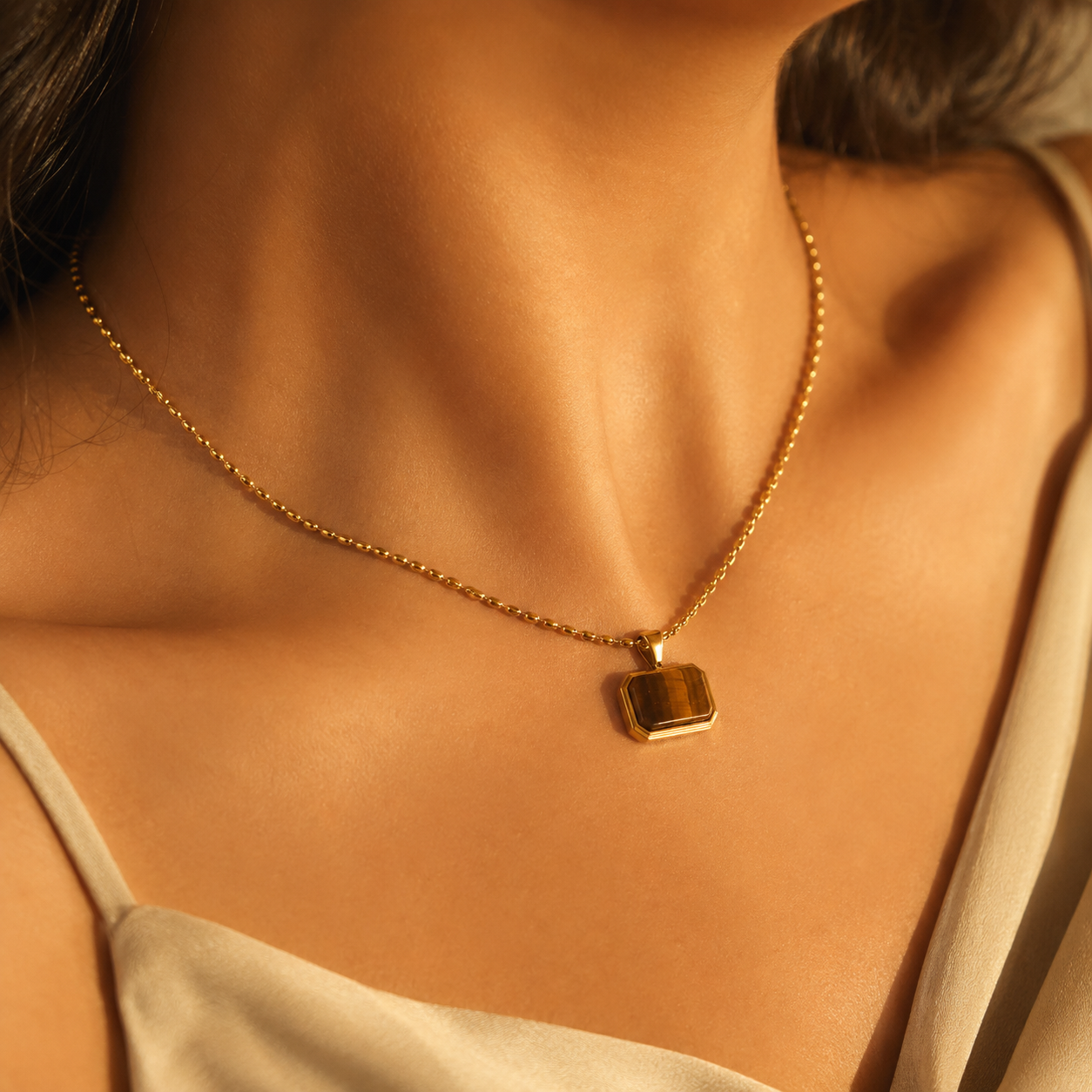 Woman wearing a gold necklace with a rectangular Tiger Eye pendant.