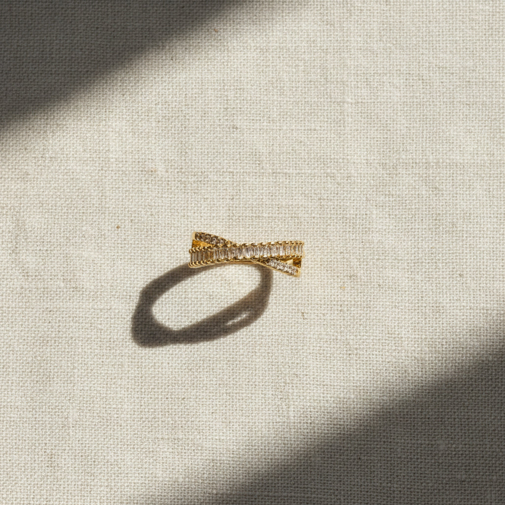 18K gold plated criss-cross adjustable CZ ring photographed on cream linen fabric