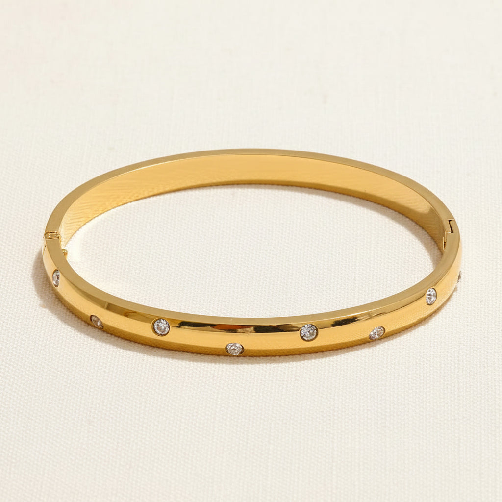 A professional standing catalogue view of the dainty, small size gold plated kada bangle with crystal paving, specifically for thin wrists, with simple shadows on a light cream background.