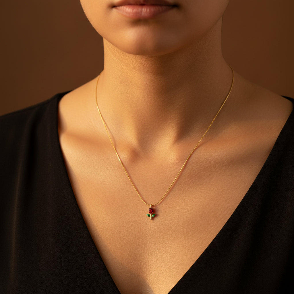 A detailed view of the Dainty Rose Pendant Necklace showing the red and green stone accents on the gold rose charm.