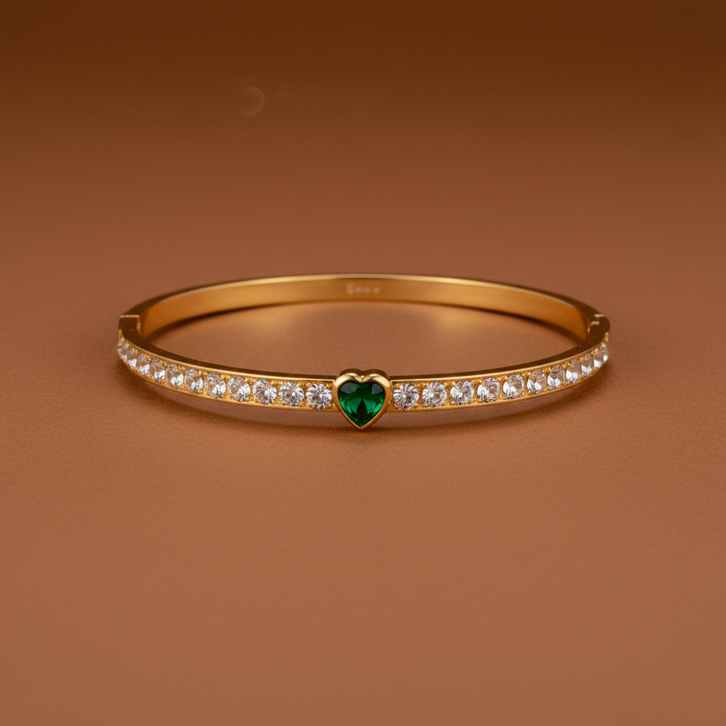 Gold bracelet with a green heart charm on a white background
