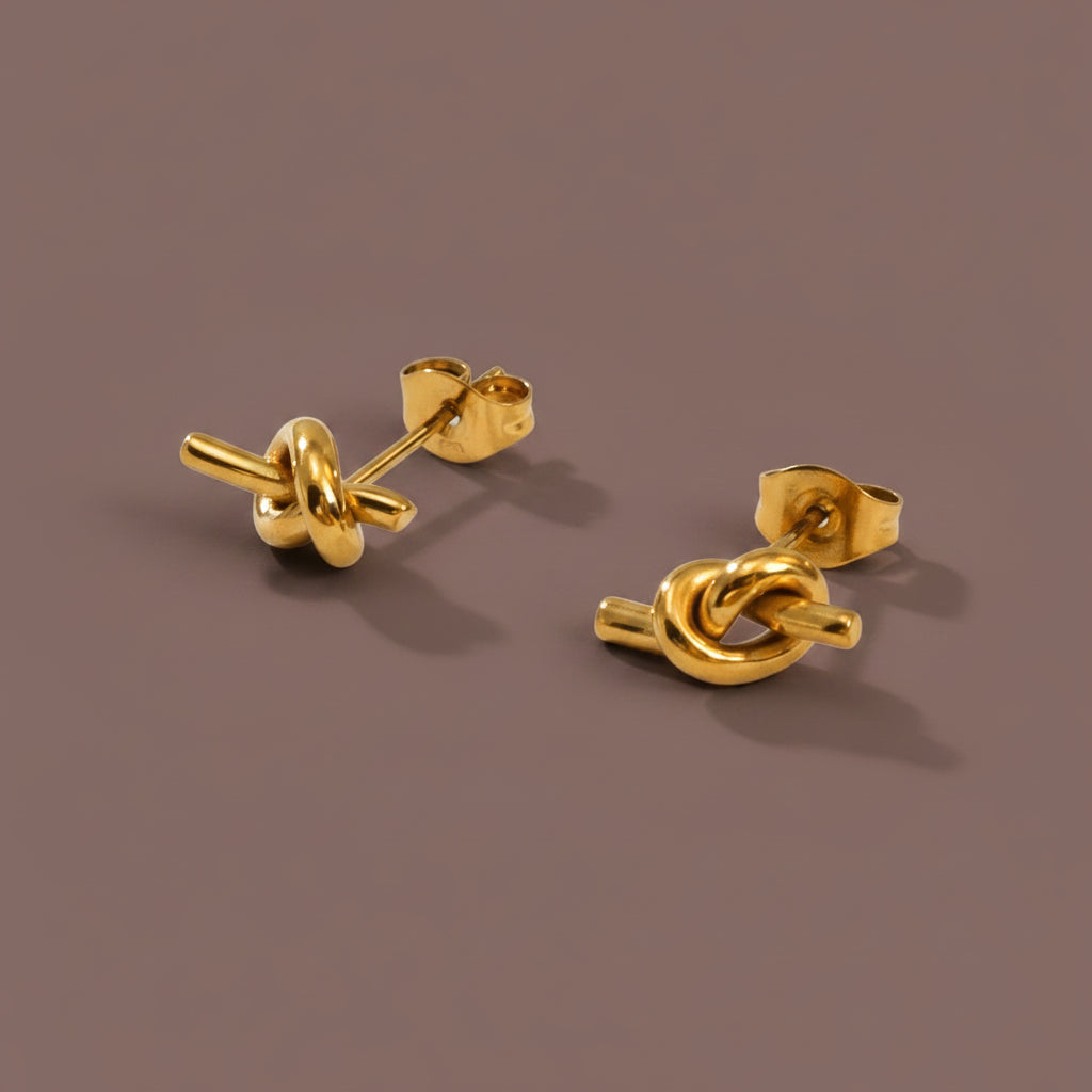 Eterna Knot Stud Earrings on a luxury #5b3b3a catalogue background.