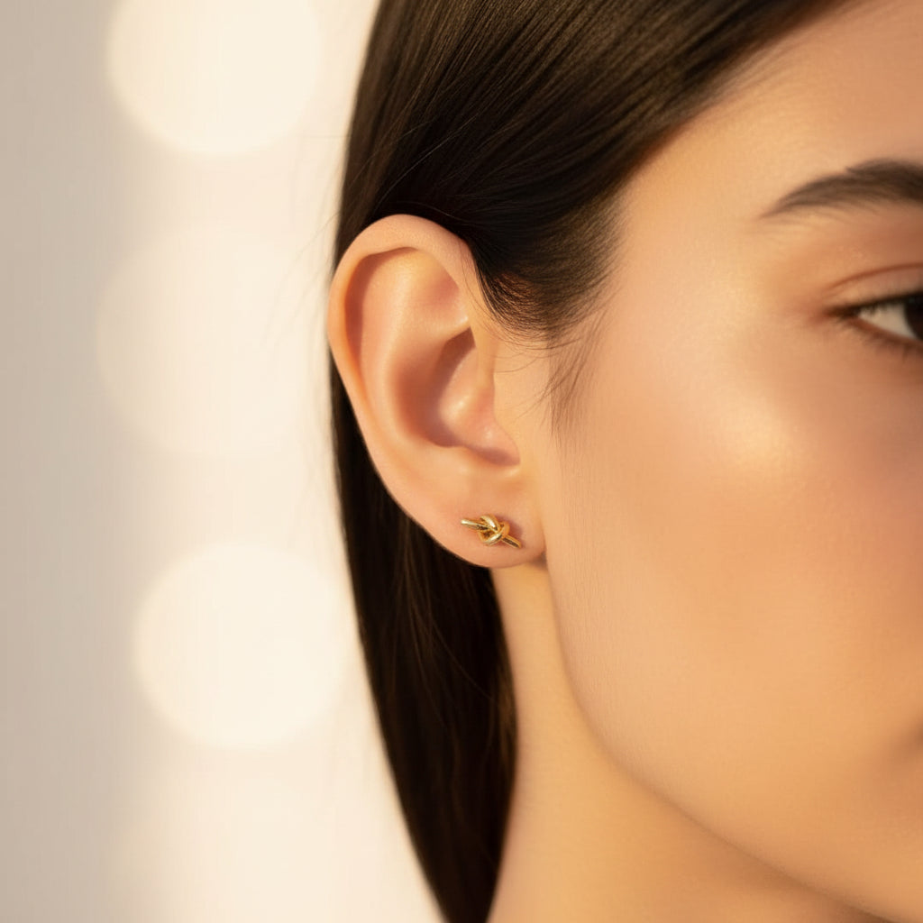 Elegant model wearing Eterna Knot Stud Earrings against a premium #f5f3eb background.