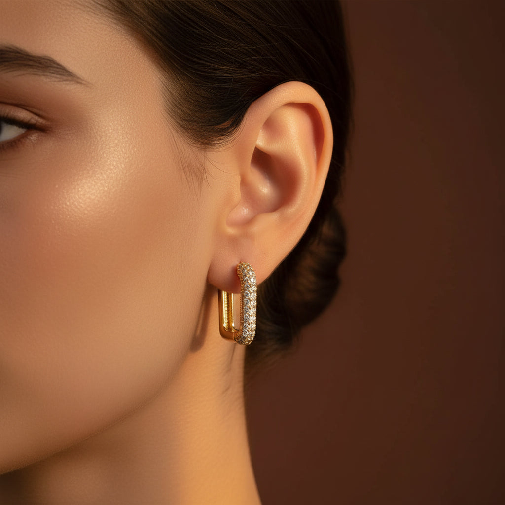 Zoomed-in lifestyle view of a model wearing the gold rectangular micro-pave crystal huggie earrings in warm golden lighting on a rich brown background.