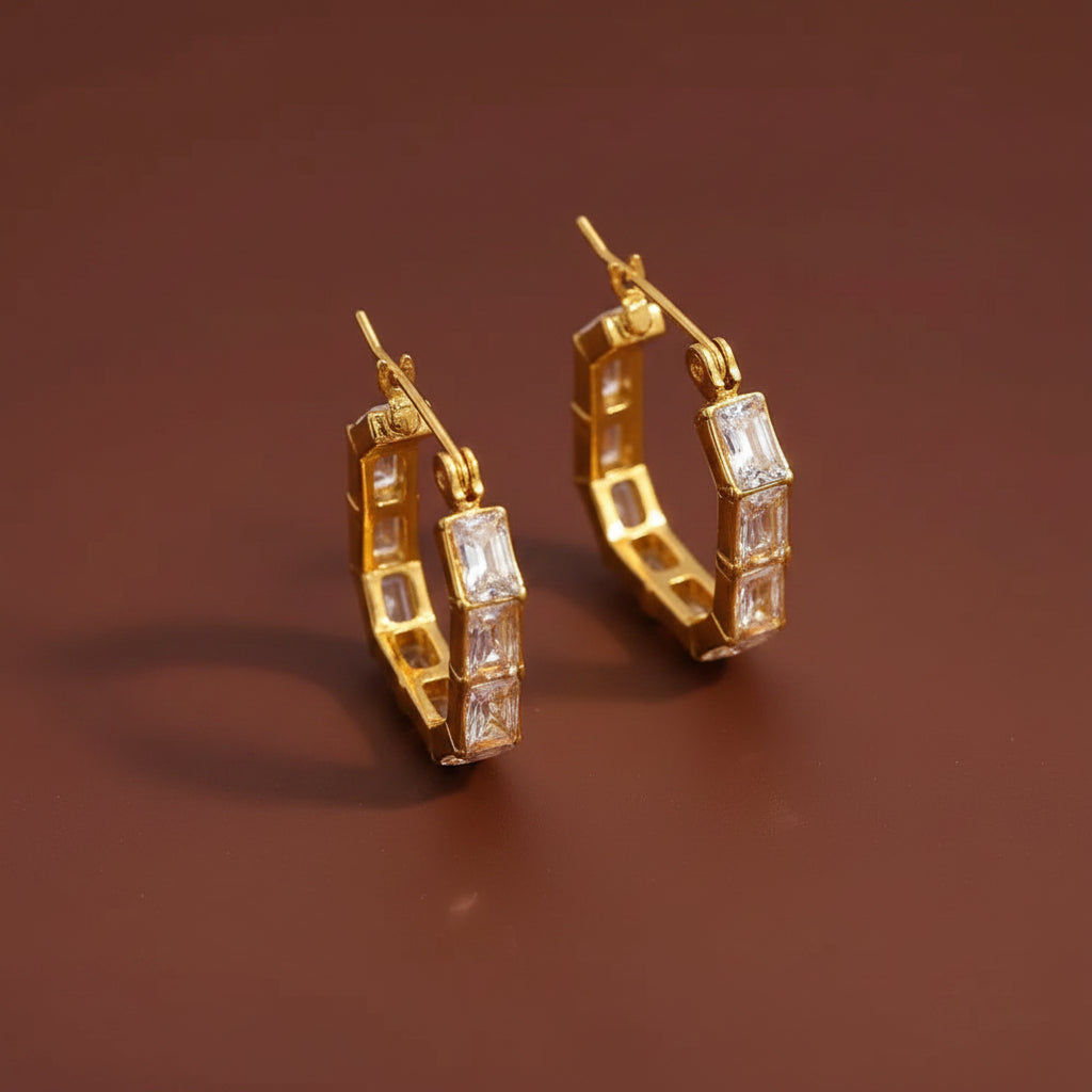 A professional flat lay catalogue shot of the gold plated geometric hexagon crystal hoop earrings with simple shadows on a rich #5b3b3a brown background.