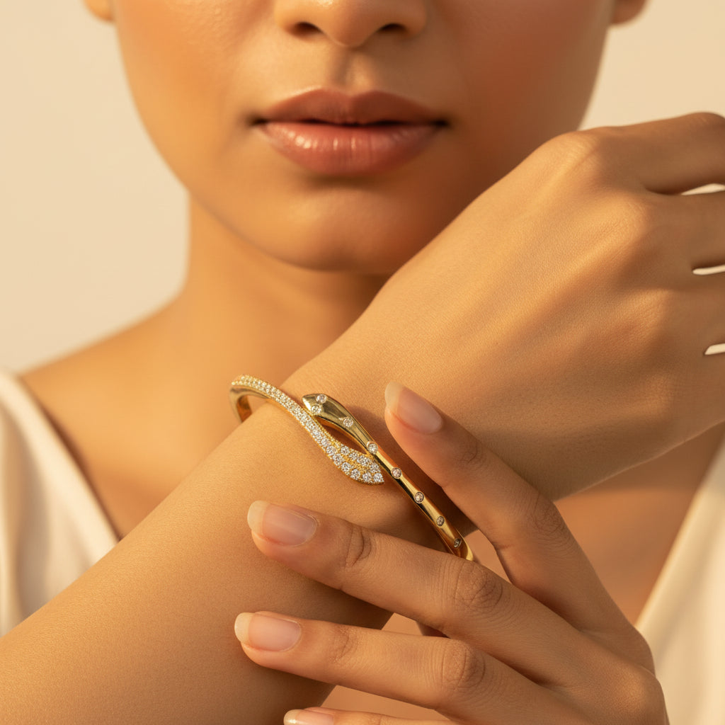 A standing profile photograph of a model with her face half-visible, showcasing the gold snake wrap bangle bracelet on her wrist under warm golden lighting against a light #f5f3eb cream background.