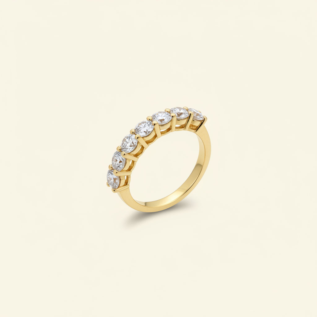 A professional standing catalogue view of the 18K gold plated seven-stone shared-prong crystal ring with simple shadows on a clean white background.