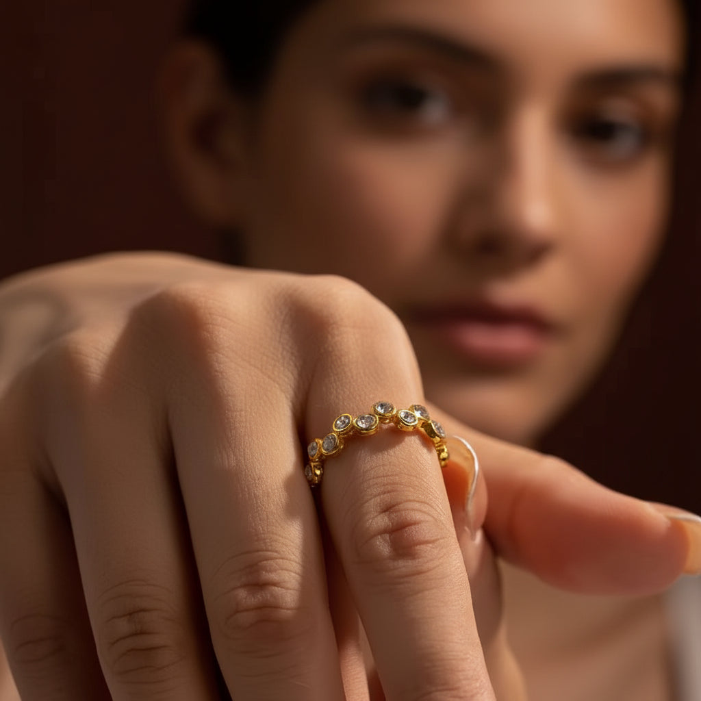 Zoomed-in flat layout of a model with her face half-visible, highlighting the gold zig-zag crystal stacker ring on her finger against a rich brown background.