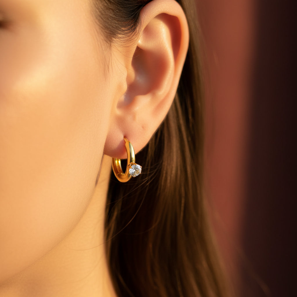Woman wearing gold solitaire huggie earrings with focus on the earrings.